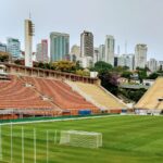 Arquibancadas e gramado do Estádio do Pacaembu, em São Paulo, com o horizonte da cidade ao fundo