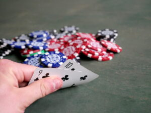 Mão segurando cartas de pôquer com fichas ao fundo, cena genérica de mesa de pôquer