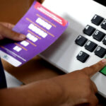 Eleitor digita voto em urna eletrônica do TSE, com folheto de instruções em braile ao lado do teclado