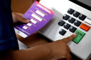 Eleitor digita voto em urna eletrônica do TSE, com folheto de instruções em braile ao lado do teclado