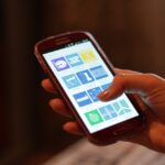 Mão segurando smartphone com tela inicial visível, uso de aplicativos em ambiente doméstico (Imagem ilustrativa: uso de smartphone, sem relação direta com o caso.)