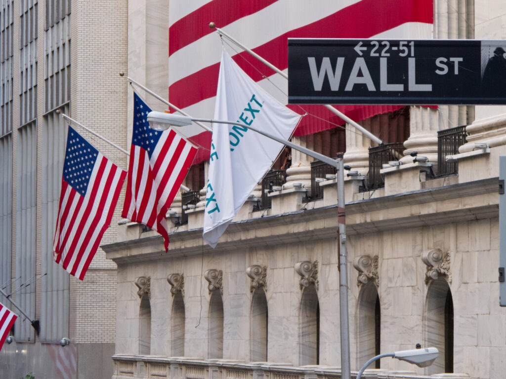 Placa da Wall Street em frente ao edifício da Bolsa de Nova York, com bandeiras dos Estados Unidos