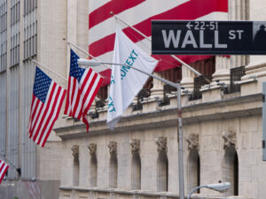 Placa da Wall Street em frente ao edifício da Bolsa de Nova York, com bandeiras dos Estados Unidos