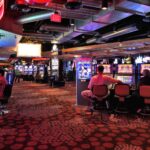 Jogadores em máquinas caça-níqueis iluminadas por luzes neon em piso de cassino