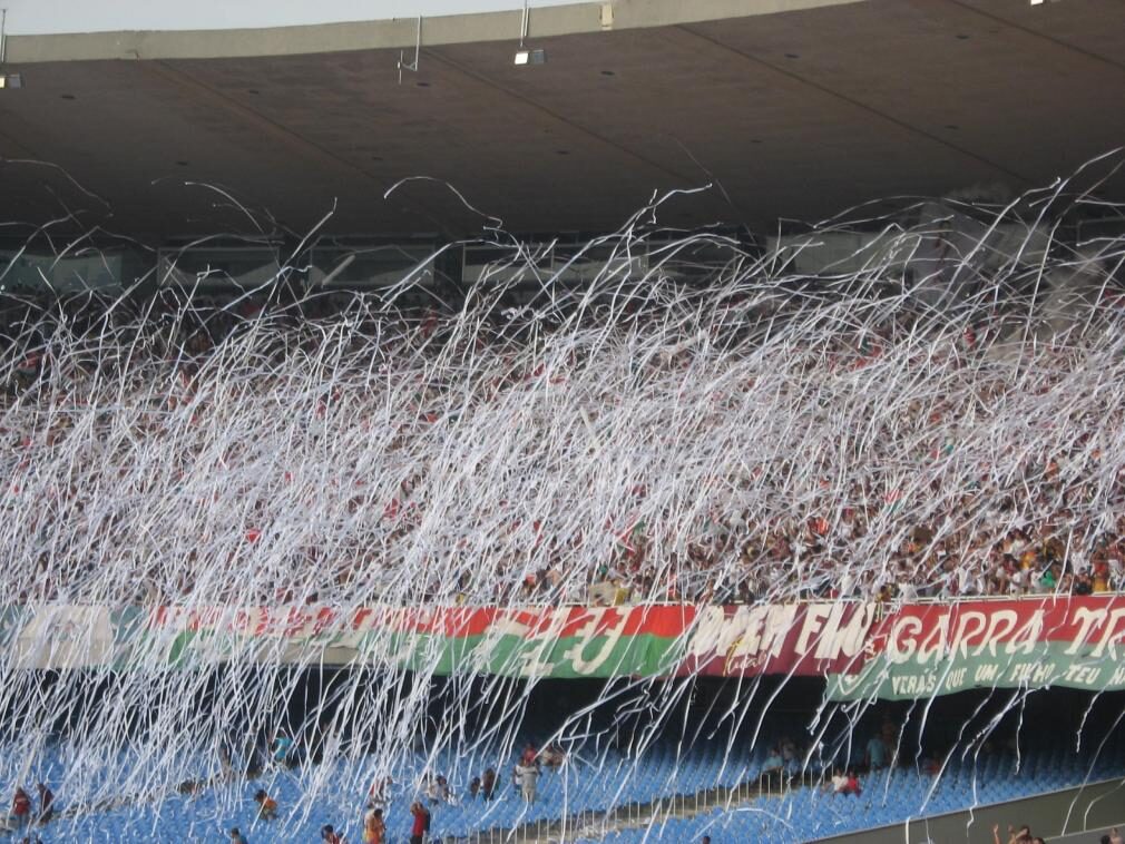 Arquibancada do Maracanã tomada por torcedores do Fluminense em meio a serpentinas brancas, com faixa tricolor ao fundo (Foto de arquivo: torcida do Fluminense no Maracanã, sem relação com jogo específico.)